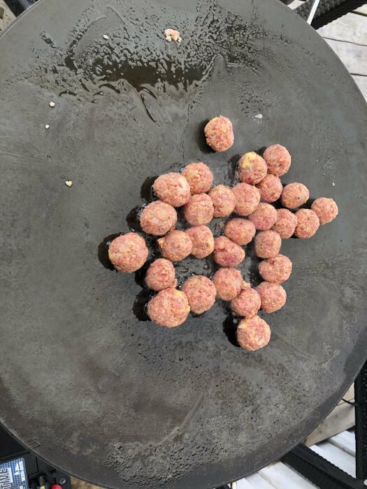 Råa köttbullar som steks på en stor stekhäll utomhus.