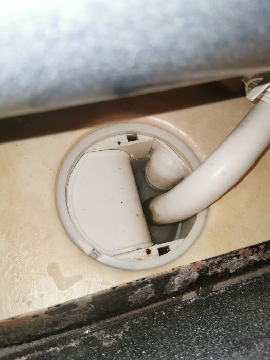 Golvbrunn i badrum med vit plastdetalj och en böjd vit slang, montering verkar vara på plats men användare upplever illaluktande problem efter städning.
