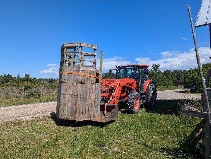 Traktor flyttar en lekställning av trä en solig dag på landsbygden.