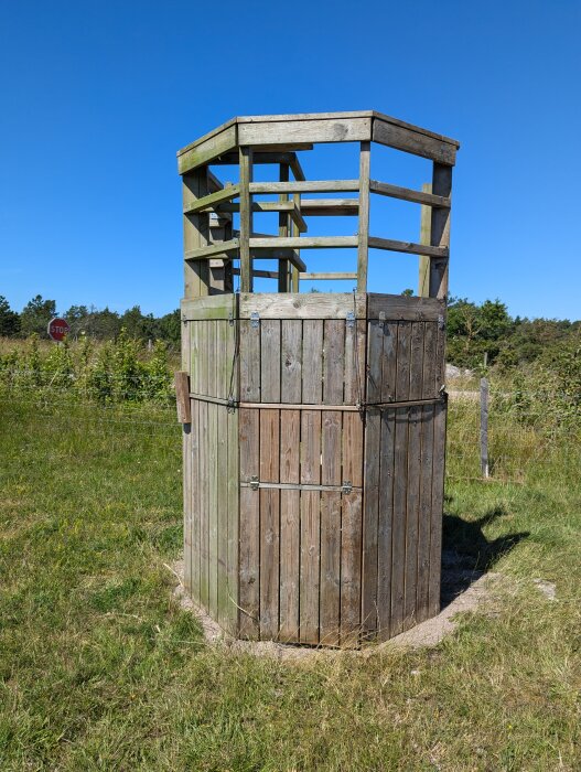 Lekställning byggd av trä med en övre och nedre sektion, omgärdad av grönt gräs och en himmel i bakgrunden. En röd stopp-skylt syns i bakgrunden.