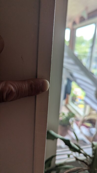 En person pekar på ett smalt mellanrum mellan en vägg och fönsterkarm med MDF-skivor istället för tjockare plankor.