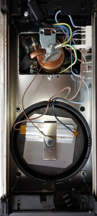 Insidan av en Moccamaster kaffebryggare med synliga värmeslingor, ledningar och komponenter. Bottenplattan har avlägsnats för inspektion.