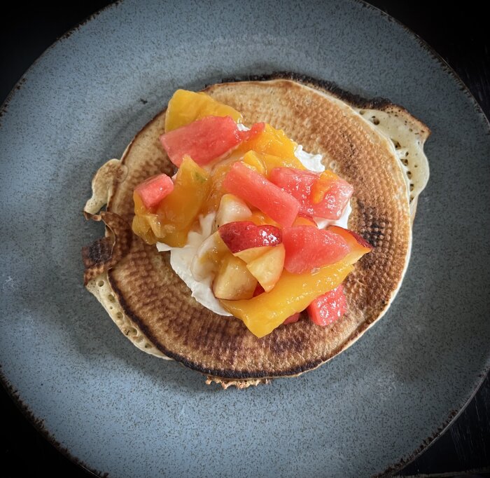 Amerikanska pannkakor toppade med fruktsallad och vispad grädde på en tallrik.