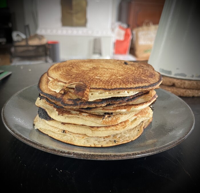 En hög med amerikanska pannkakor på en tallrik, serverade till semesterlunch. Bakgrunden visar ett kök med köksutrustning och väskor.