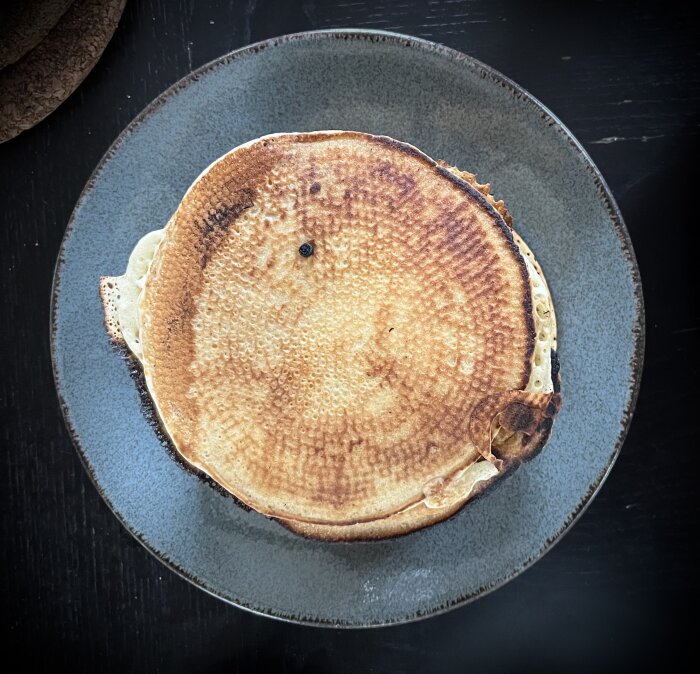 En tallrik med tre amerikanska pannkakor, serverad på ett mörkt bord.