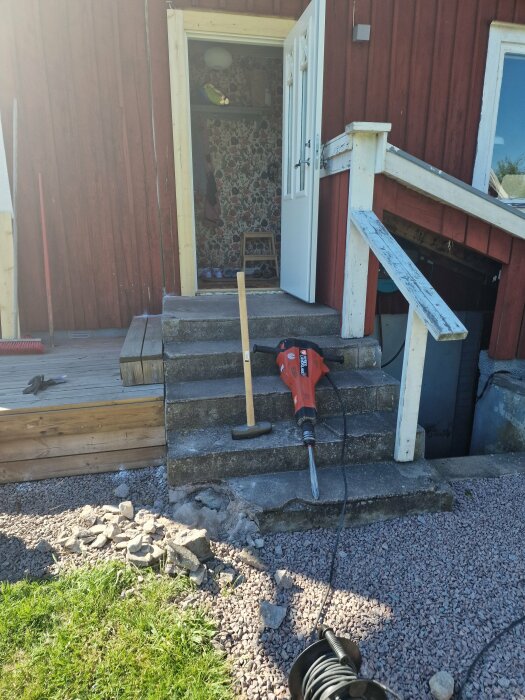 Trappa med verktyg och betongsprickor framför en öppen husentré under renovering.