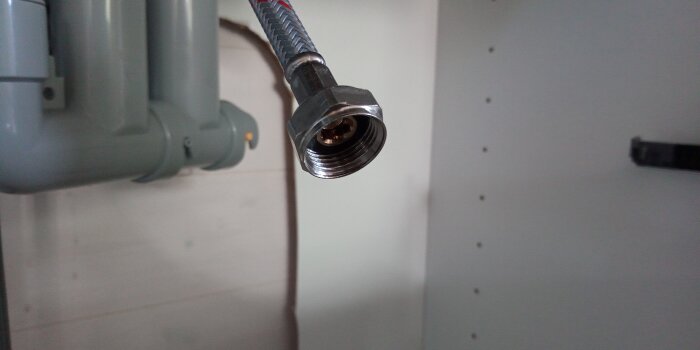 Kopplingsdetalj av en vatette 2 rörs väggbricka monterad under diskbänk, med PEX-slang och lös mutter nära avlopp.