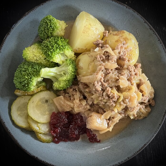 Tallrik med kålpudding, kokt potatis, kokt broccoli, inlagd gurka och en klick lingonsylt.