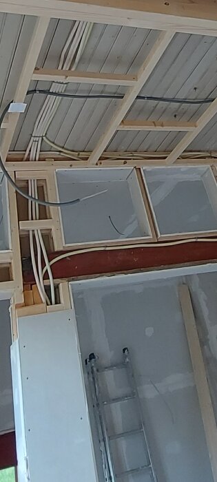 Kablage för elektrisk installation synligt genom ramkonstruktionen i taket av ett renoverat rum med en stege lutad mot väggen.