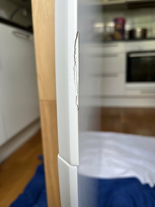 Närbild på en skada med spricka på kanten av en vit möbel i en köksmiljö.