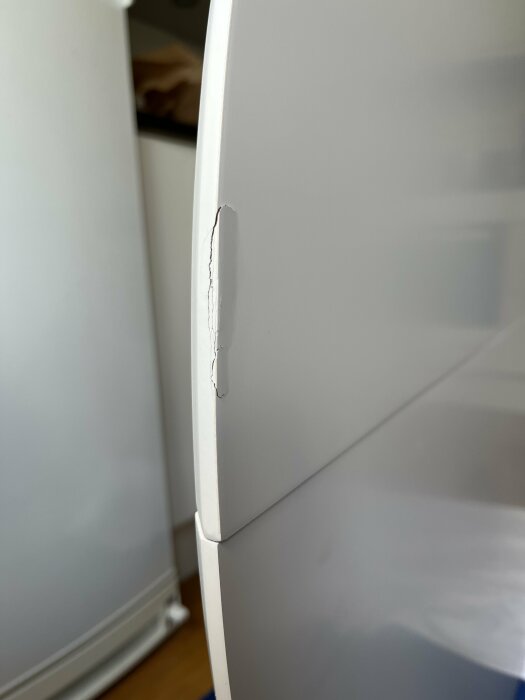 Närbild av en skada på ett vitt bord, där en bit av kanten har spruckit och lossnat.