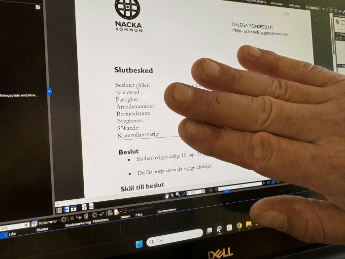 Hand över bygghandlingar från Nacka Kommun på en datorskärm. Texten visar slutbesked från miljö- och stadsbyggnadsnämnden för ett byggprojekt.