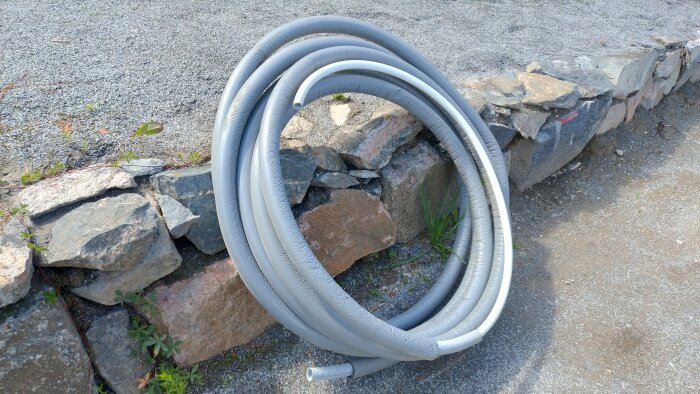 15,5 meter av isolerat 25mm pex rör-i-rör för vatten och värme, av märket LK, ligger ihoprullat mot en stenmur utomhus.