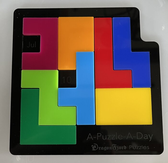 Färggrant pussel av plastblock i olika former på en svart ram med texten "A-Puzzle-A-Day" och "DragonFjord Puzzles" samt datumet "Jul 10".