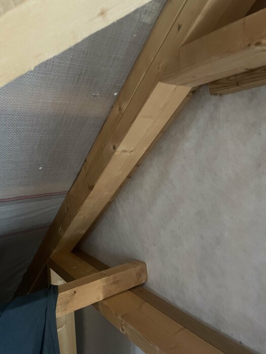 Takstol och reglar på en oinredd övervåning, täckt med plast och vindpapp, som ska isoleras med polyuretan-isolering.