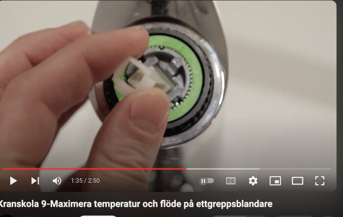 Hand placerar en vit plastdel i en öppnad köksblandare med grön tätning, från en video om att maximera temperatur och flöde på ettgreppsblandare.