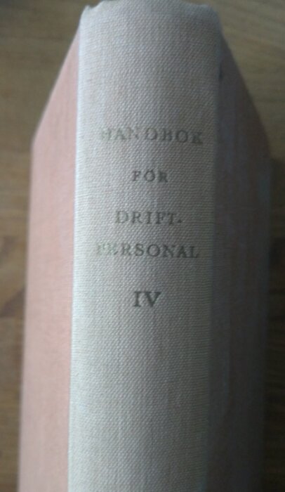 En handbok med titeln "Handbok för driftpersonal IV" på en trähylla.