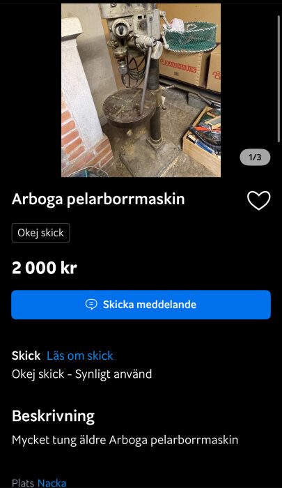 Äldre pelarborrmaskin av märket Arboga, placerad i ett rum med tegelvägg och flera kartonger och verktyg runtomkring. Synligt använd och i okej skick.