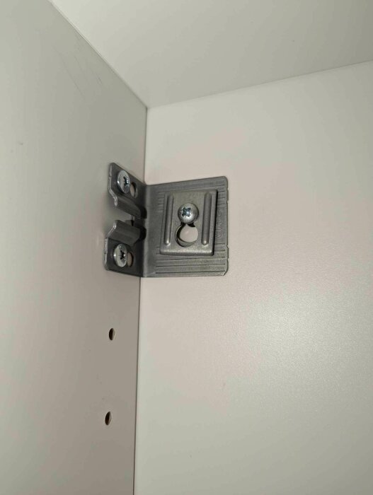 Närbild på ett hörnfäste inne i ett badrumsskåp med två synliga skruvar, fäst vid en vit skåpvägg.