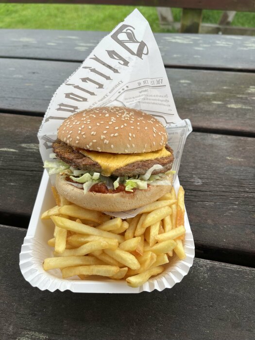 En taco-burgare med pommes frites serverade på ett papperstallrik utomhus på en väderbiten träbord.