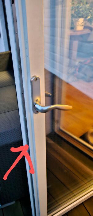 Handtag på en vit altandörr där låset verkar vara defekt och inte stänger ordentligt, med en röd pil som pekar mot låsområdet.