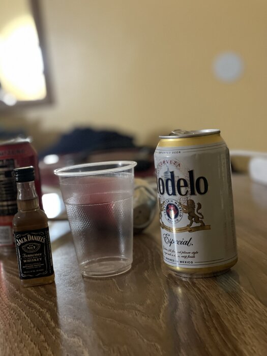 Ölburk av märket Modelo, plastglas och miniflaska med Jack Daniel's whiskey på ett bord i ett rum med gul vägg.