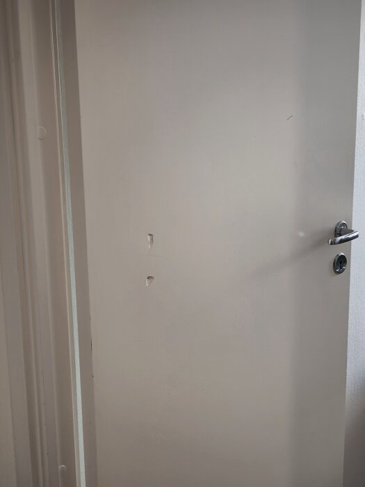 Vit innerdörr med två mindre gropar eller hål i mitten av dörrbladet nära dörrhandtaget.