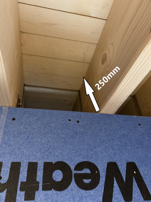 Närbild av en takventilation i en carport där öppningen är cirka 250 mm, med en pil som visar måttet, omgiven av träväggar och ett blått skyddslager.