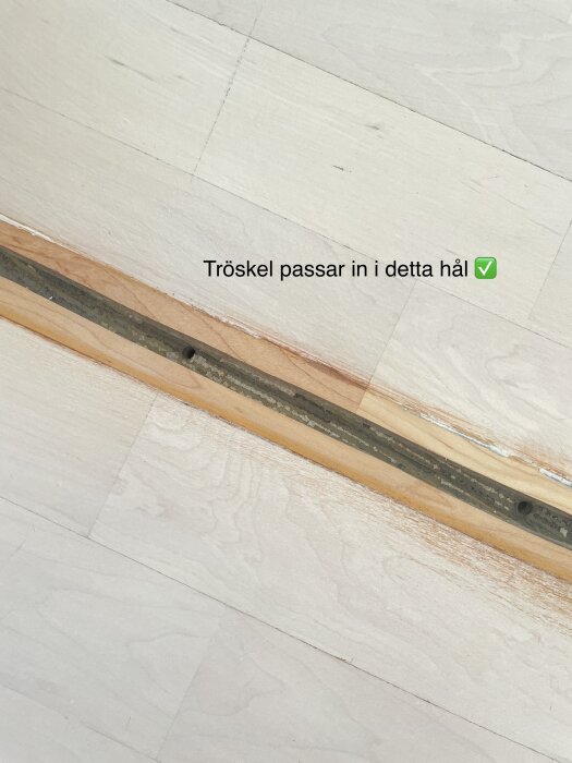 En bred dörrtröskel har avlägsnats och lämnat ett smalt, avlångt hål i trägolvet, med markeringen "Tröskel passar in i detta hål ✅" på bilden.