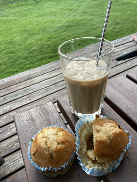 Likör 43 med is i ett glas med en metallsugrör och 1,5 blåbärsmuffins på ett träbord utomhus, gräsmatta i bakgrunden.