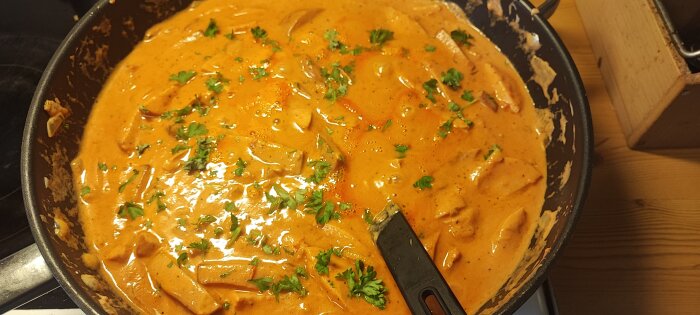 Panna med krämig korvstroganoff, garnerad med hackad persilja, redo att serveras med basmatiris.