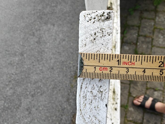 Närbild av en vitmålad träbräda som mäts med en linjal, visar cirka 2 cm tjocklek.