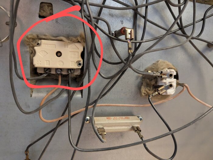 Baksidan av en ugn med kablar och komponenter, en täckplåt är borttagen. En del omgiven av en röd cirkel visar anslutningar och identifierande märkning.