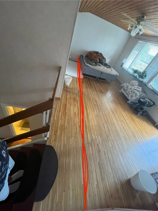 Vy ovanifrån av ett rum med trägolv och en dubbelsäng. På golvet finns röda streck som markerar var bjälklaget är delat.