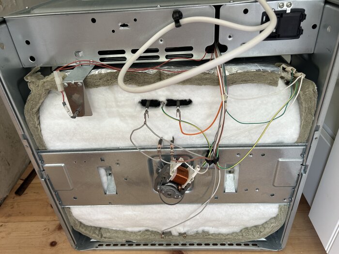 Bakpanelen av en ugn med synliga elektriska komponenter och kablar.