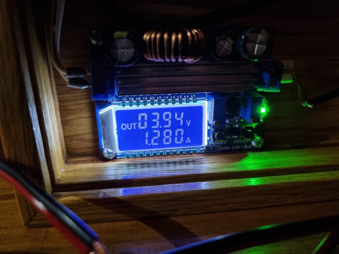 Digital voltmeter och amperemeter på en spänningsomvandlare som visar 3,94V och 1,28A, kopplad till belysning i ett bygge.