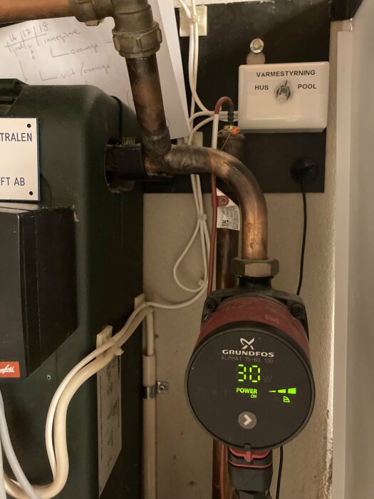 Värmepump med en inkopplad brytare märkt "Värmestyrning Hus/Pool". Märkesskylt på pumpen visar "Grundfos Alpha1". Sladdar och rör anslutna.