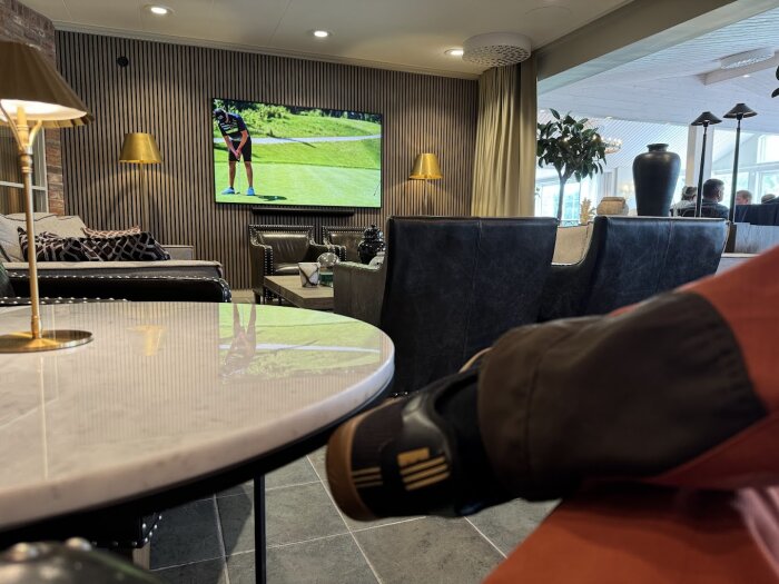 En mysig kaféhörna med sköna stolar, lampor och en stor TV som visar golf. Bilden är tagen efter en renovering som gjorde utrymmet större.