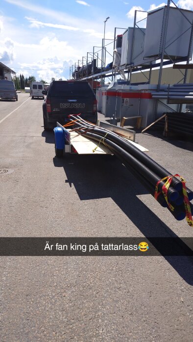 En pickup med en släpvagn full av långa rör är parkerad på en industriell plats under en klar himmel. Text på bilden: "Är fan king på tattarlass😂".