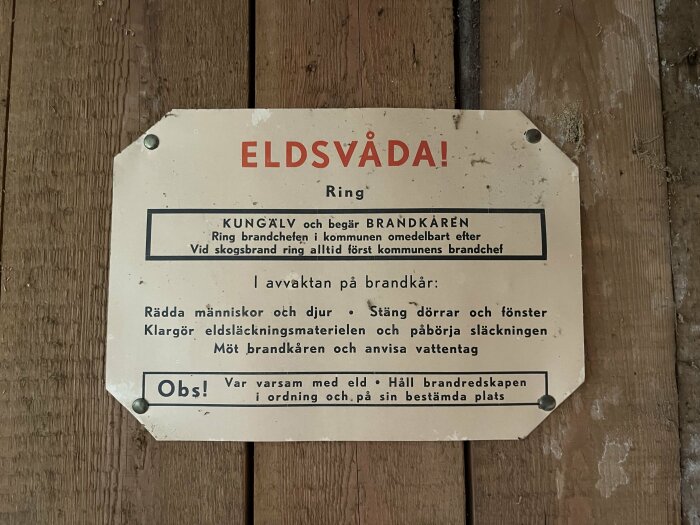 Gammal brandskylt från Kungälv uppsatt på en trävägg i ett hus från 1938, med instruktioner för hur man hanterar eldsvåda och kontaktar brandkåren.