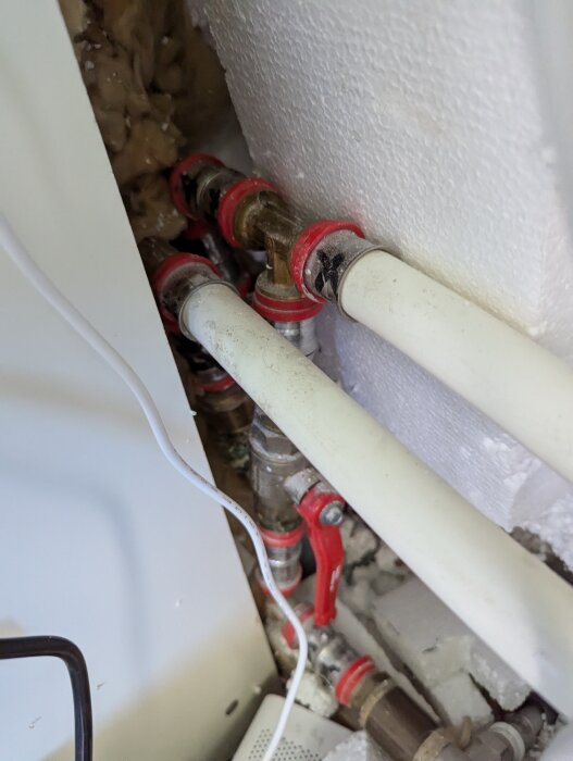 Två plastbelagda rör med röda ventiler anslutna till en vägg med några andra kopplingar i ett skåp för fjärrvärme.