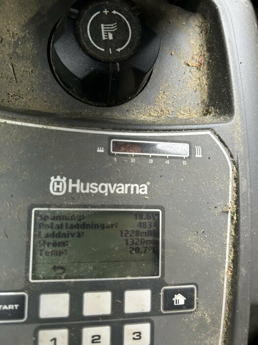 Display på Husqvarna Automower visar spänning 18,6V, total laddningar: 483, laddnivå: 1228mAh, ström: 1320mA, temp: 20,7°C, med smutsig yta och knappar.