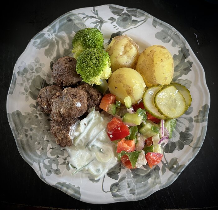 En tallrik med köttbullar, färskpotatis, broccoli, fetaostsallad, inlagd gurka och tzatziki.