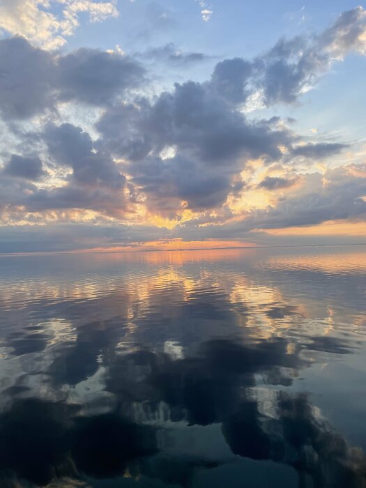 Solnedgång över Vättern med moln som speglas i det stilla vattnet.