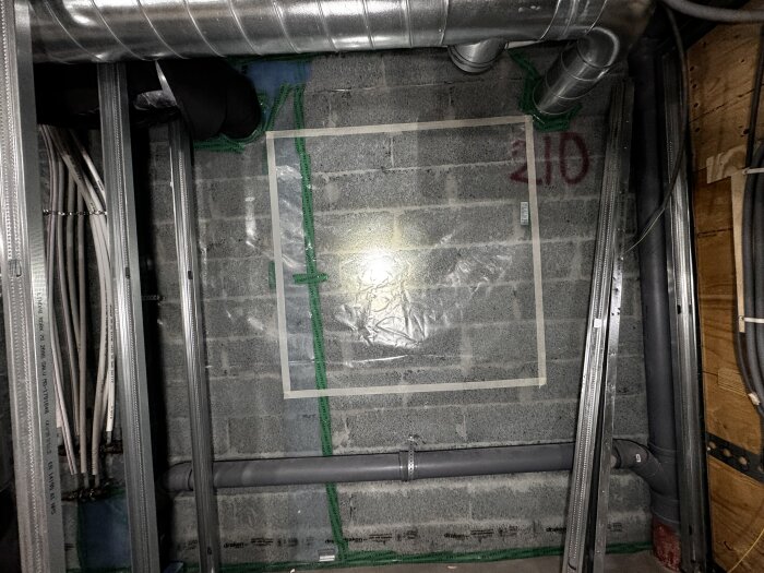 Källarvägg av lecablock med ångspärr och stålreglar, synliga rörledningar och isolering, samt en del av ventilationssystemet.