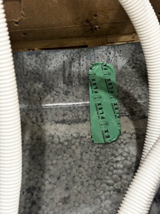 Fukt och kondens på ångspärr monterad mot lecablock i en källarvägg, med grönt fuktskyddstejp och vita rör i förgrunden.