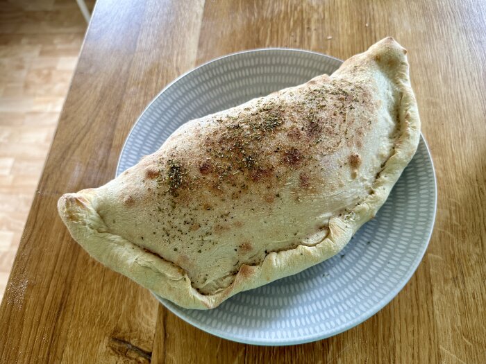 Calzone pizza på en tallrik på ett träbord, rester från gårdagen.