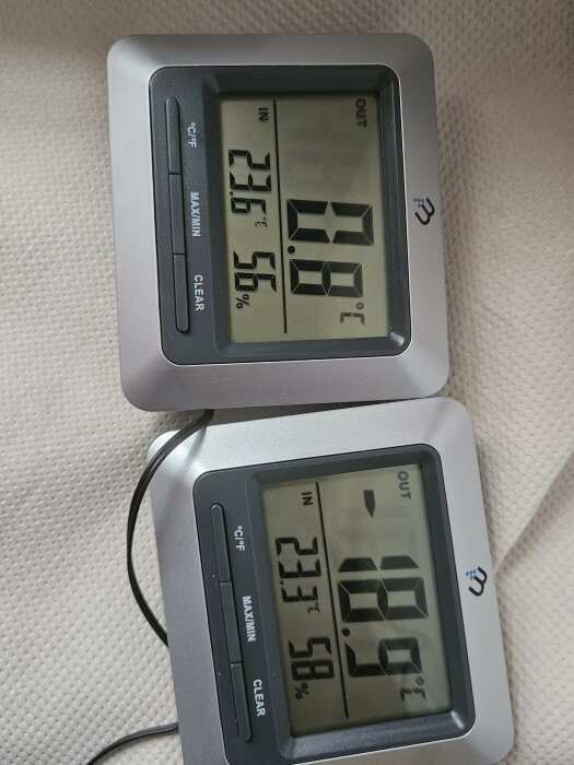 Två digitala termometrar visar en innetemperatur på 23,6°C och 23,1°C samt en utetemperatur på 0,0°C och -18,0°C med respektive luftfuktighet på 55% och 56%.