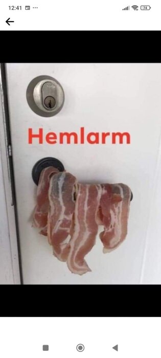 Bilden visar en dörr med ordet "Hemlarm" och skivat bacon hängande på dörrhandtaget.
