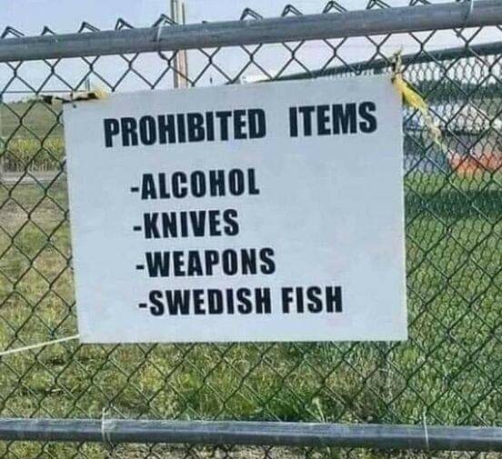 Skylt på stängsel med texten "PROHIBITED ITEMS: -ALCOHOL -KNIVES -WEAPONS -SWEDISH FISH," som förbjuder alkohol, knivar, vapen och godiset Swedish Fish.